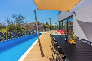 Ein Poolbereich mit Holzterrasse, einem Tisch mit Stühlen und einem Glasgefäß mit Früchten und einer Flasche.