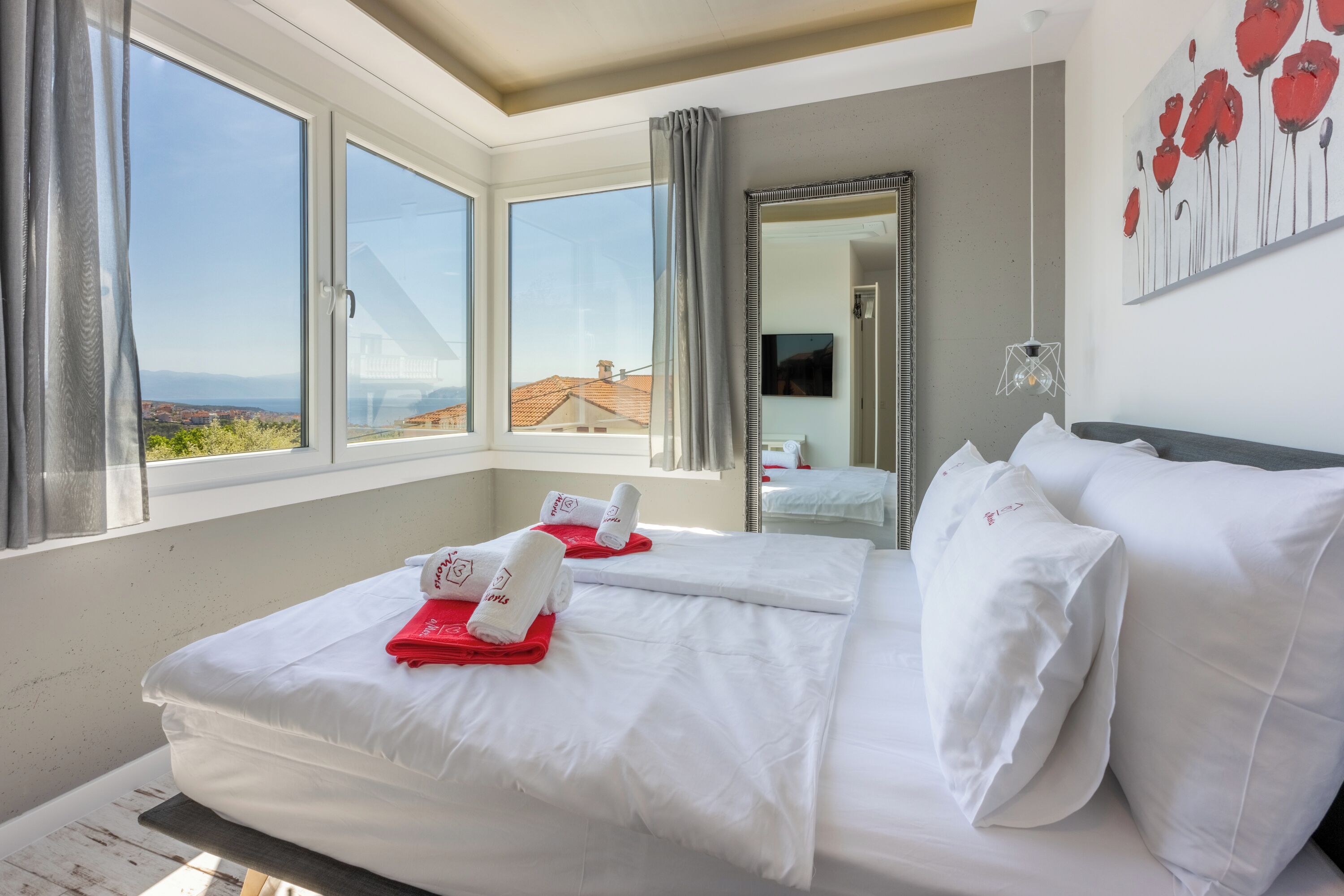 A hotel room with a large bed, a view of the city, and a painting on the wall.