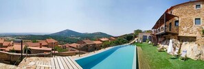 Une piscine avec une terrasse en bois, des bâtiments en pierre et une montagne en arrière-plan.