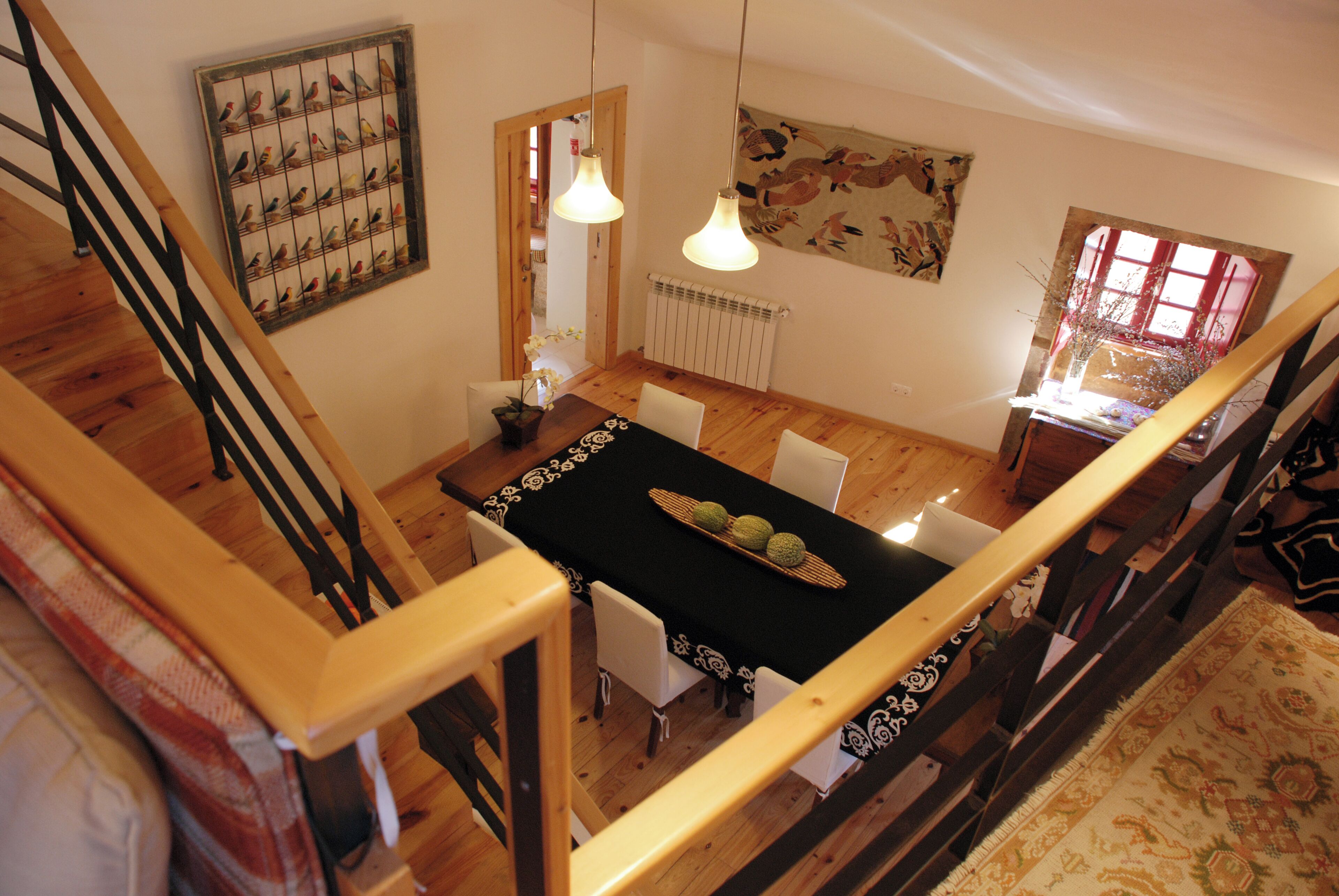A dining area with a black tablecloth, white chairs, wooden flooring, and a staircase with wooden railings.