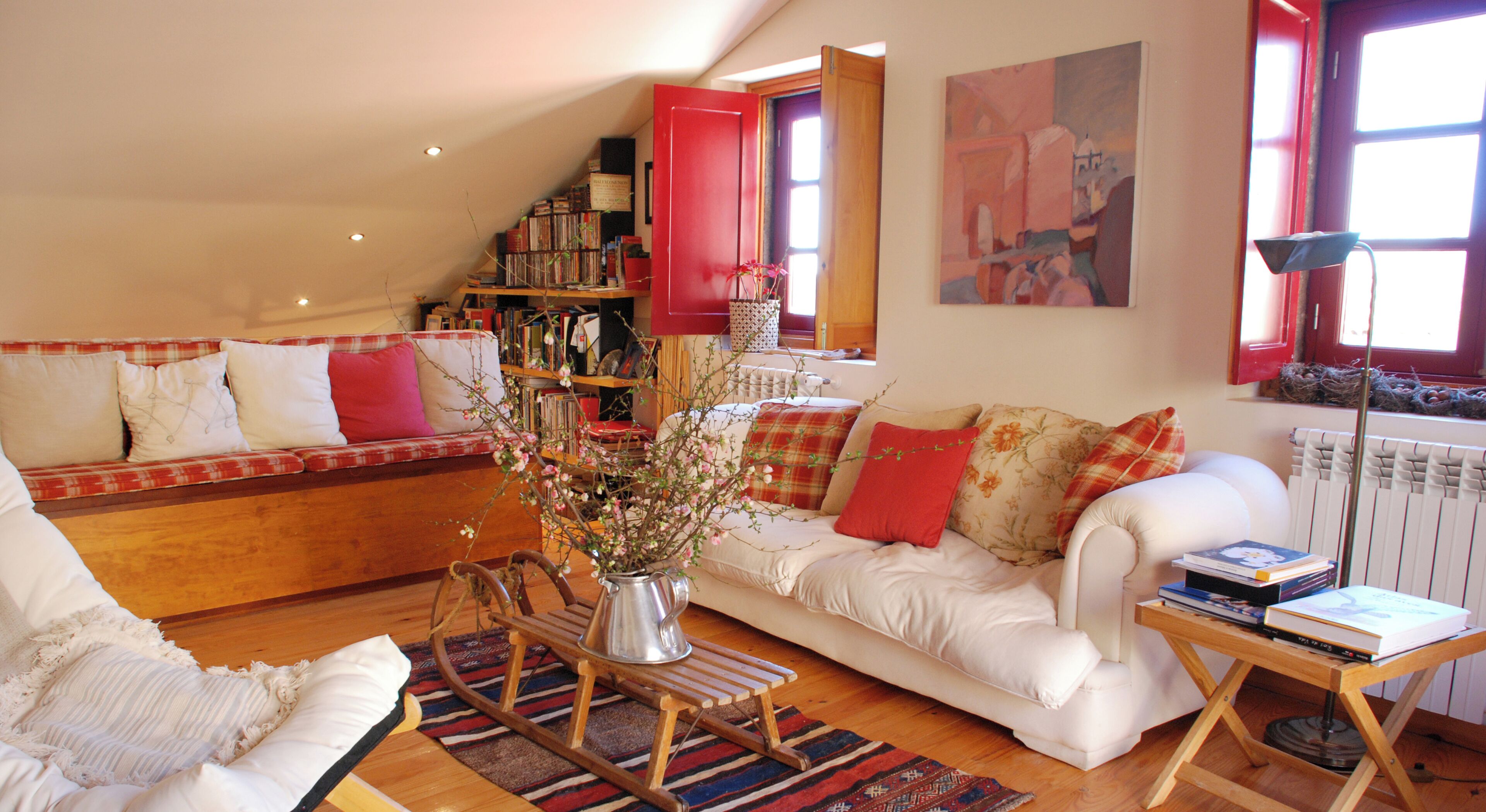 A cozy living room with a white sofa, a wooden rocking chair, a bookshelf, and a radiator.