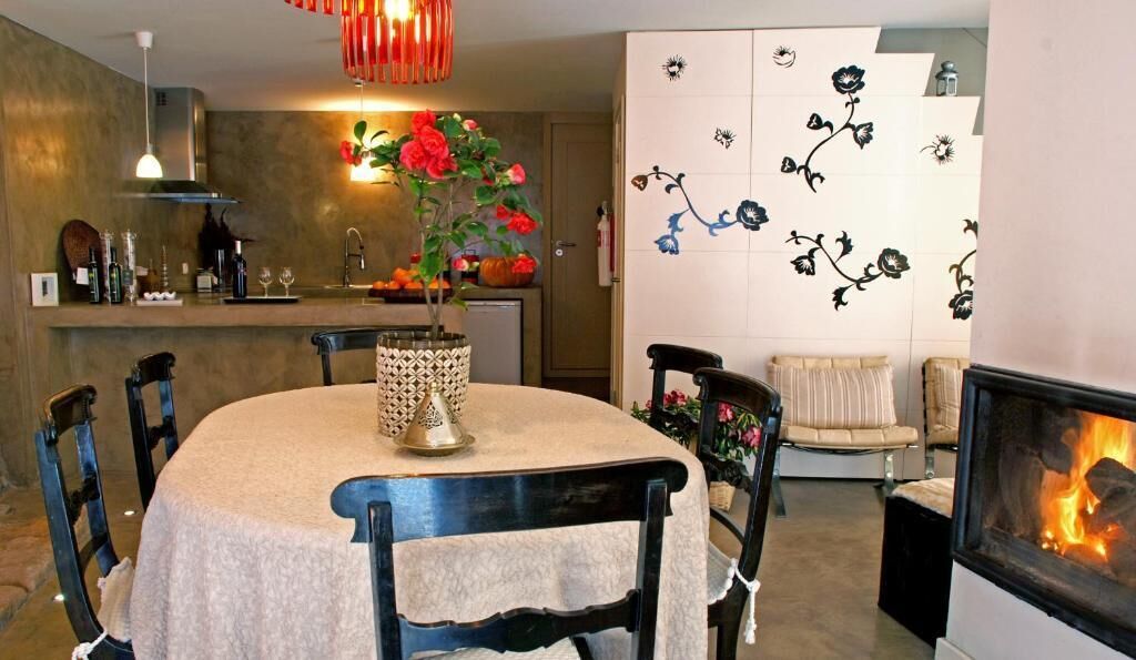 Een eethoek met een ronde tafel, stoelen, een vaas met bloemen, een open haard en een wand met bloemendecoratie.