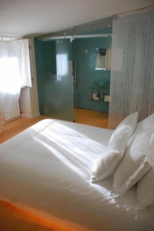 Une chambre à coucher avec un lit, une salle de bain avec une douche et une porte vitrée donnant sur une autre pièce.