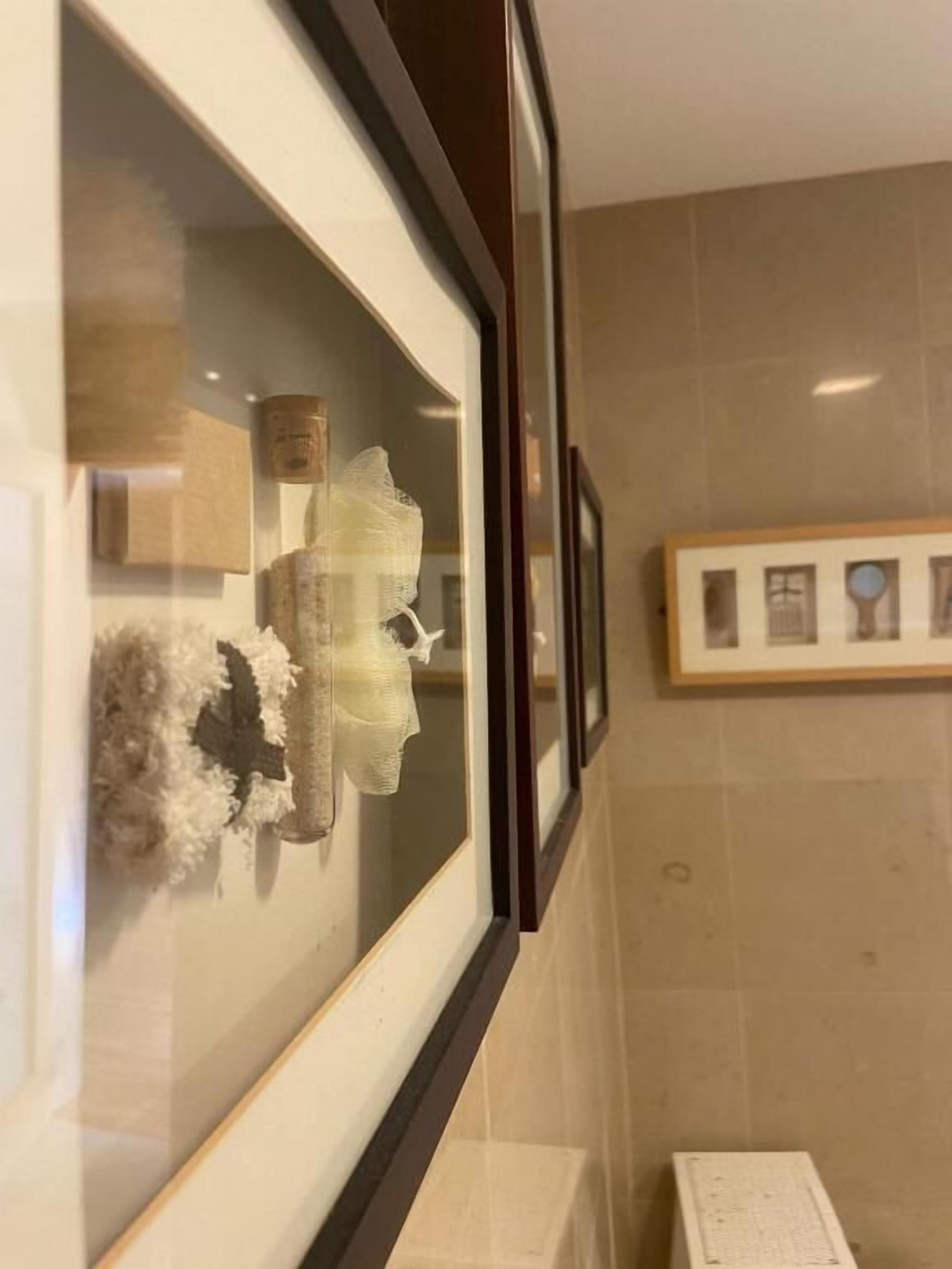 A framed artwork on a wall, a framed picture above it, and a tiled wall.