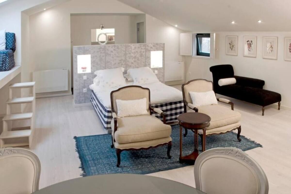 A modern bedroom with a bed, two armchairs, a small table, and a sofa.