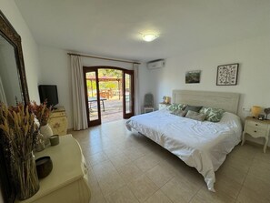 Een slaapkamer met een bed, een bureau, een stoel, een spiegel en uitzicht door een glazen deur op een buitenruimte.