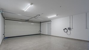 A clean, empty garage with a closed garage door, fluorescent lighting, and a wall-mounted electrical box. - Standard Villa 2 - Casangular by Upper (Adeje)