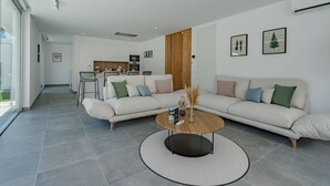 A modern living room with a sofa, coffee table, and kitchen in the background. - Standard Villa 2 - Casangular by Upper (Adeje)
