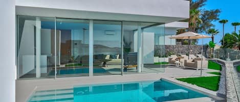 Una casa moderna con piscina cubierta por vidrio, asientos al aire libre y un muro de piedra.