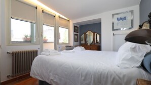 Habitació d'hotel amb un llit, un radiador, una finestra amb persianes, un calaixera, un mirall i una fotografia a la paret.