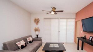 Ein Wohnzimmer mit Sofa, Couchtisch, Deckenventilator, Fernseher und einer Schiebetür.