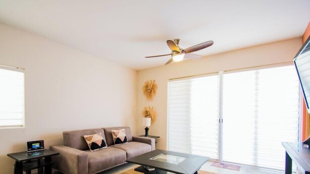 Ein Wohnzimmer mit einer Couch, einem Couchtisch, einem Deckenventilator und einem Fernseher.