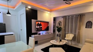 A modern living room with a glass dining table, white sofas, a TV, and a ceiling light fixture. - Welcome to Lucky7suites (Parañaque)