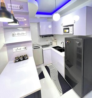 A modern kitchen with white cabinetry, a black refrigerator, a microwave, and a coffee machine. - Welcome to Lucky7suites (Parañaque)