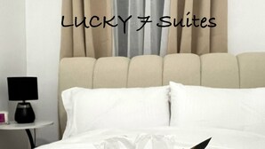 A neatly made bed with white linens, a black and gold striped towel, and a bottle of lotion. - Welcome to Lucky7suites (Parañaque)