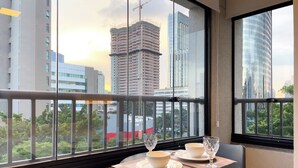 Ein Essbereich mit Tisch für zwei Personen, ein Balkon mit Metallgeländer und Blick auf Stadtgebäude.