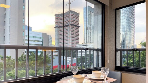 Uma sala de jantar com uma mesa posta para dois, uma varanda com guarda-corpo de metal e vista para edifícios da cidade.