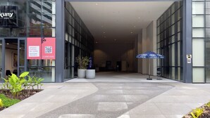 Entrada de um edifício moderno com portas de vidro, placa indicando uma loja e um código QR.