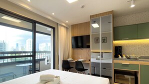 Quarto de hotel com cama, escrivaninha, cadeira, TV, cozinha e vista para a cidade.