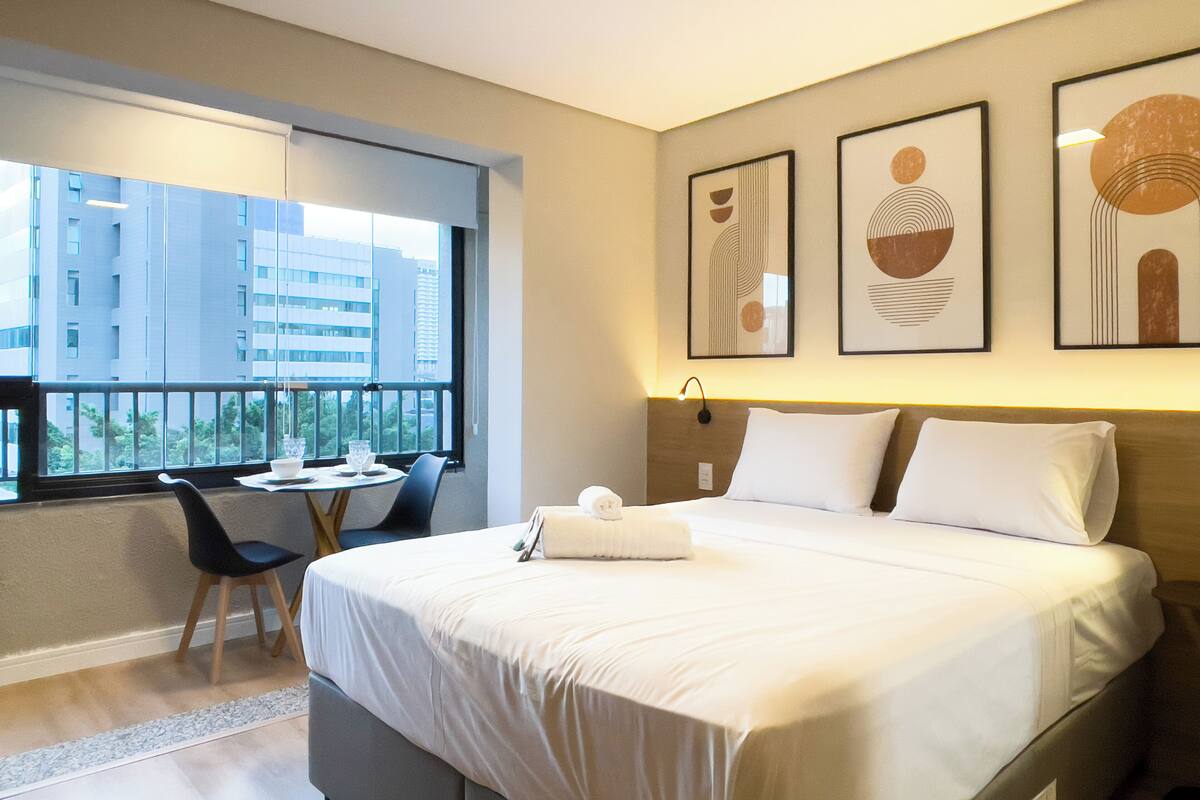 Habitación de hotel con cama, escritorio, silla y ventana con vista a edificios.