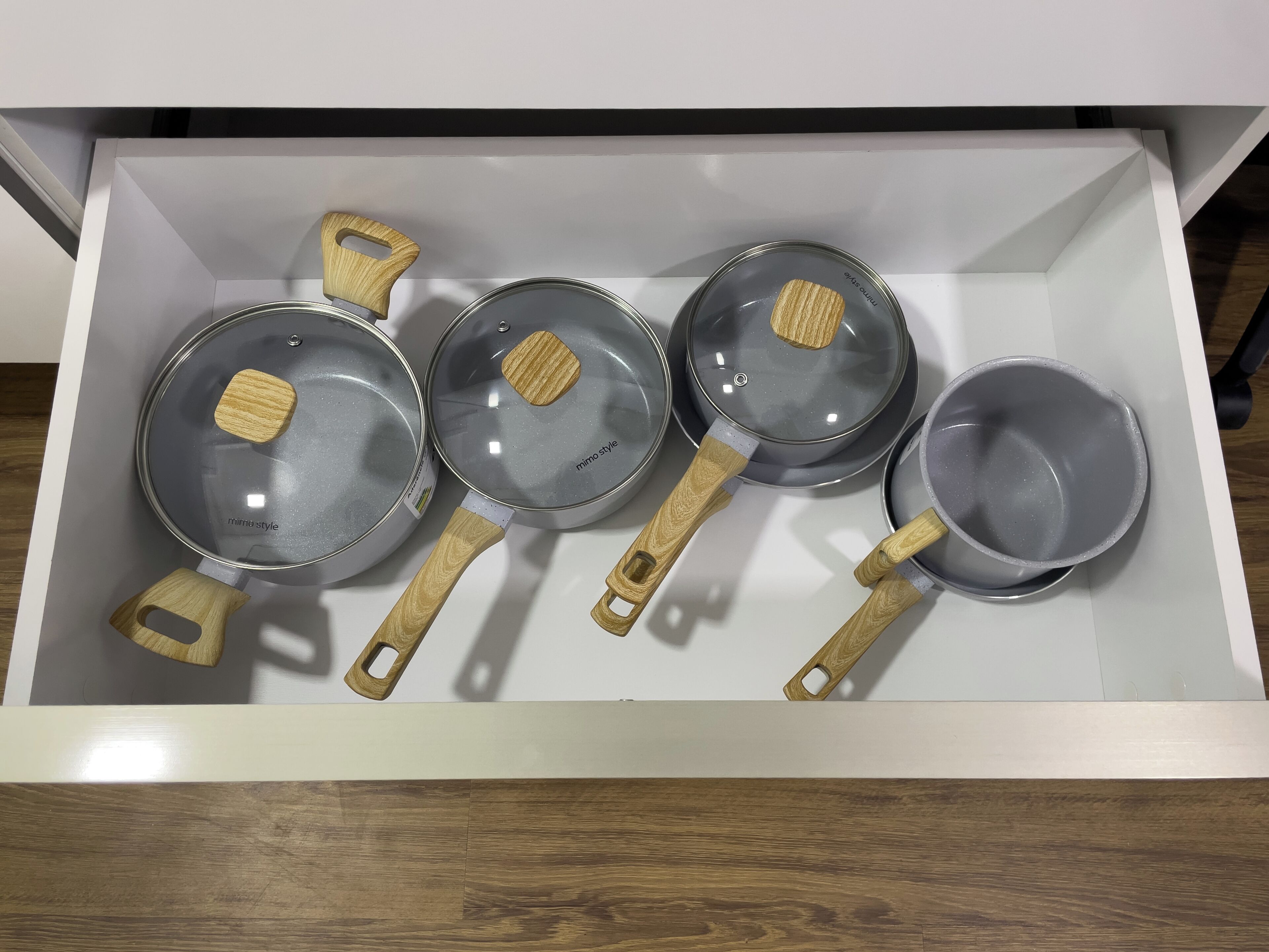 Eine Schublade mit vier Kochpfannen und einem kleinen Salatbecken, jeweils mit Holzgriffen.