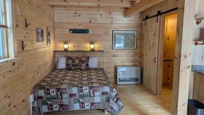 Une pièce de style cabane en bois, avec un lit, deux lanternes fixées au mur, une carte encadrée et un radiateur.