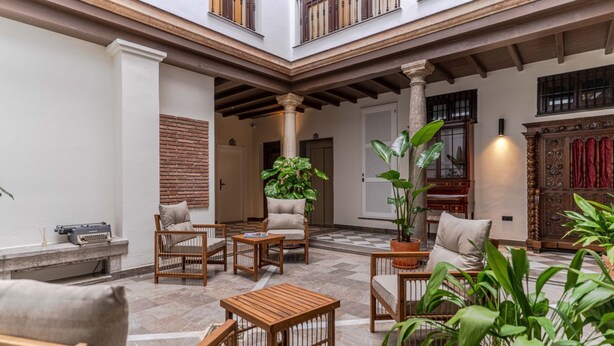 Un patio amplio con muebles de madera, plantas en macetas y una columna central.