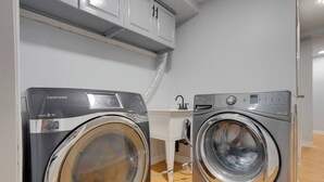 Ein Waschraum mit zwei Waschmaschinen mit Frontlader, einem weißen Waschbecken und einem Schrank darüber.