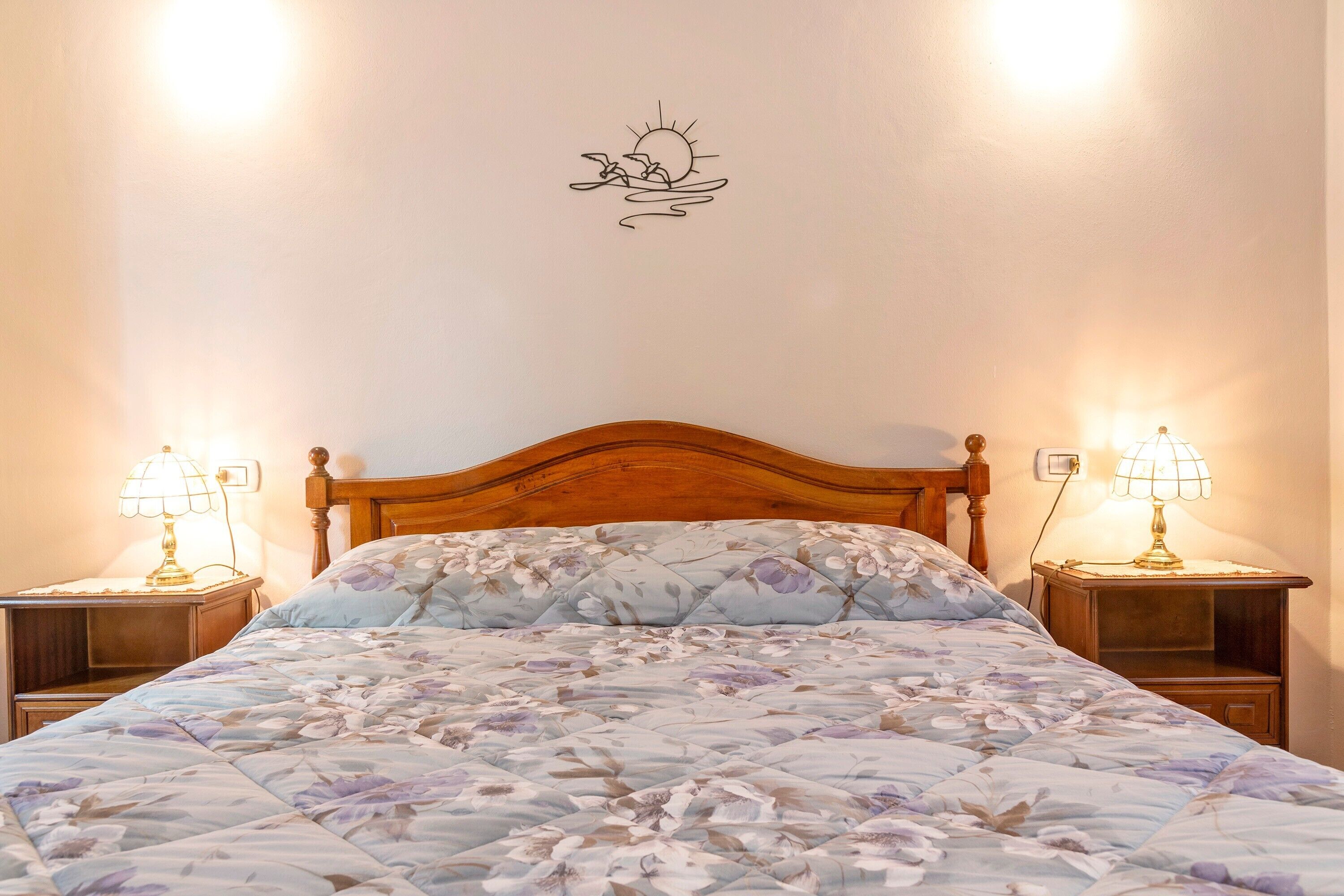 Ein Schlafzimmer mit hölzernem Kopfteil, floralem Bettbezug, zwei Nachttischlampen und einer Wanddekoration.