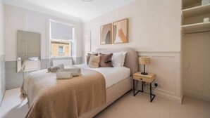 Une chambre à coucher avec un lit, une table de chevet, une lampe et une œuvre d’art accrochée au mur.