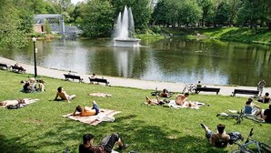 Ein Park mit einem Brunnen, Bänken und Menschen, die entspannt im Gras liegen.
