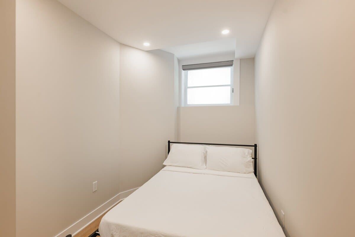 A small, narrow room with a single bed, a window, and a ceiling light.