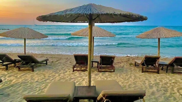 A beach with lounge chairs and thatched umbrellas.