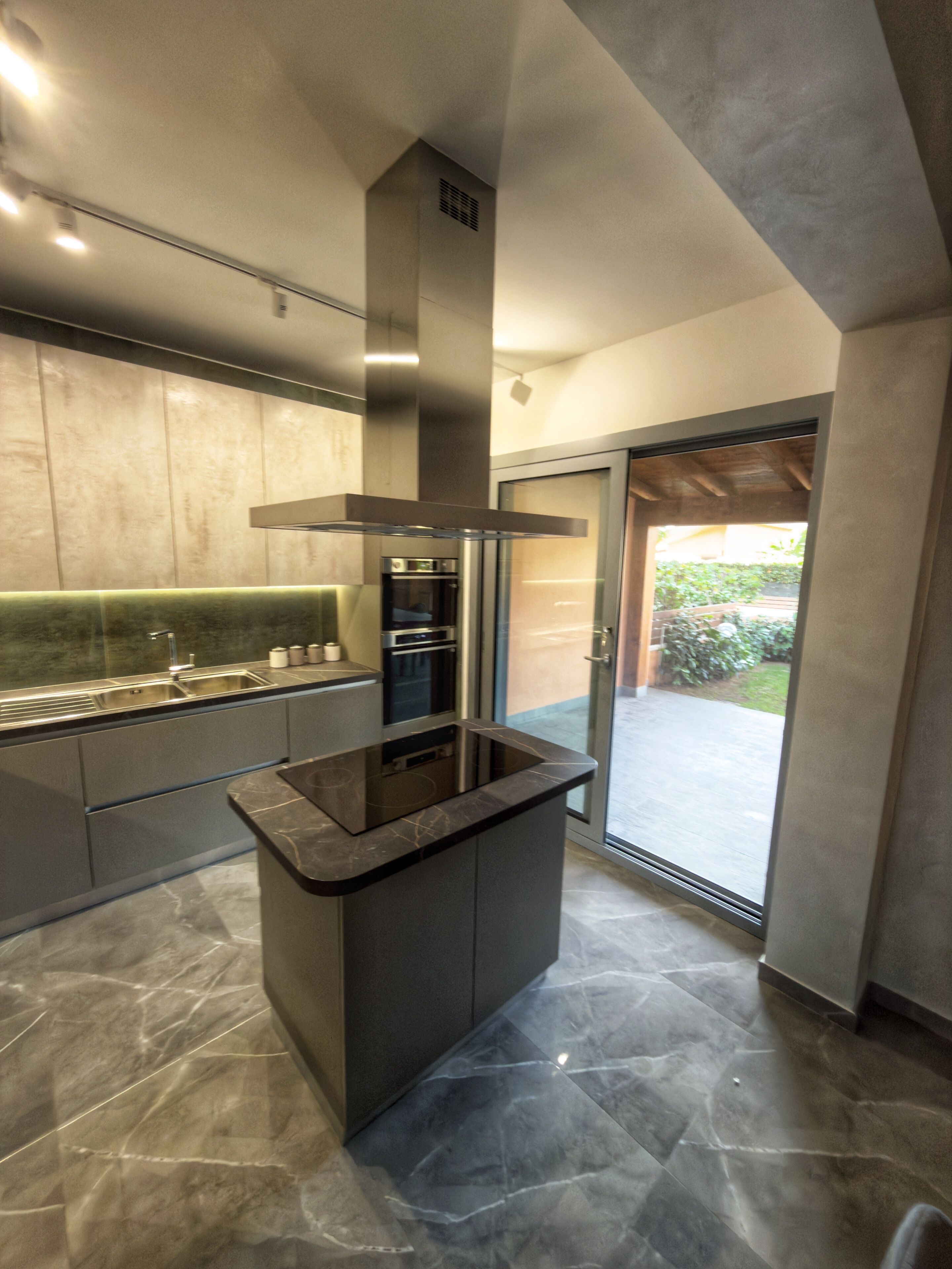 Een moderne keuken met een centraal eiland, roestvrijstalen apparatuur en uitzicht op buiten.