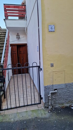 A residential building with a gated entrance, a wooden door, and a balcony with red railings.