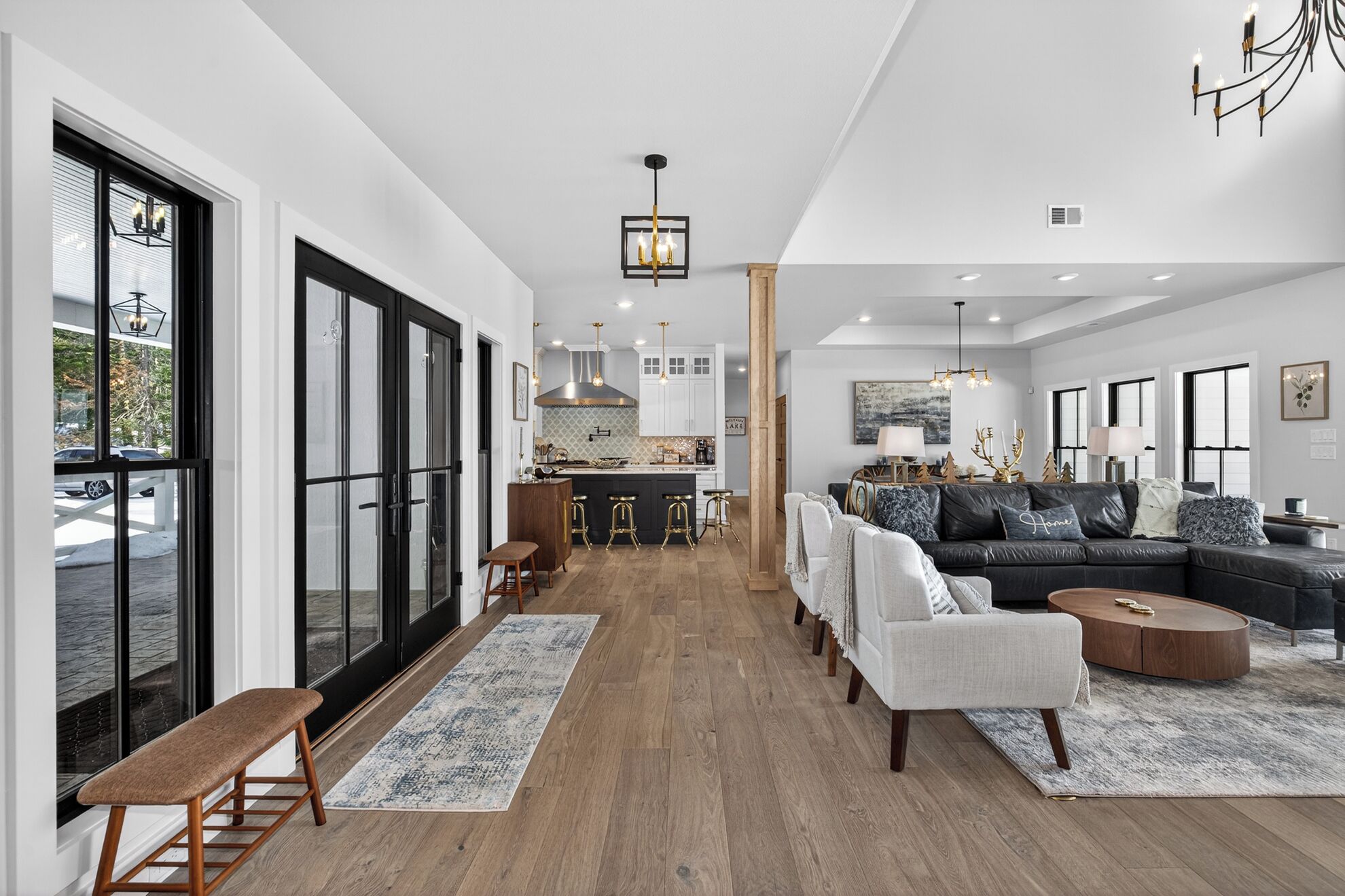 A spacious living room with a large sofa, a coffee table, and a bench. There is a kitchen area with a bar and stools.