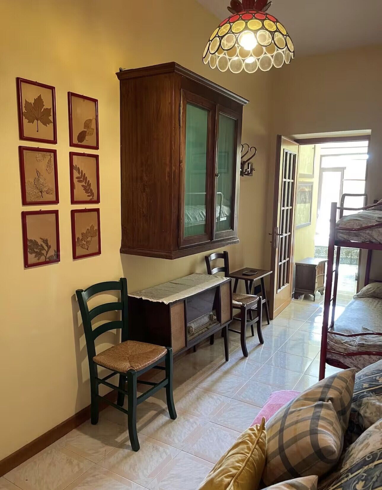 A room with a wooden cabinet, framed botanical prints on the wall, a television, and a bed.