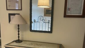 A vintage dresser with floral designs, a lamp, and framed certificates on the wall.