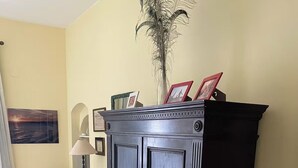 A room with a dark wooden cabinet, a chair, a lamp, and a painting on the wall.