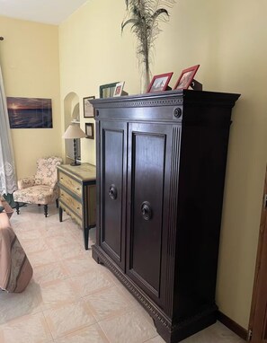 A room with a dark wooden cabinet, a chair, a lamp, and a painting on the wall. - Lo Studio Di Gabriella (Bolsena)