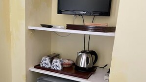 A compact kitchenette with a small refrigerator, a kettle, and a flat-screen TV mounted above a shelf.