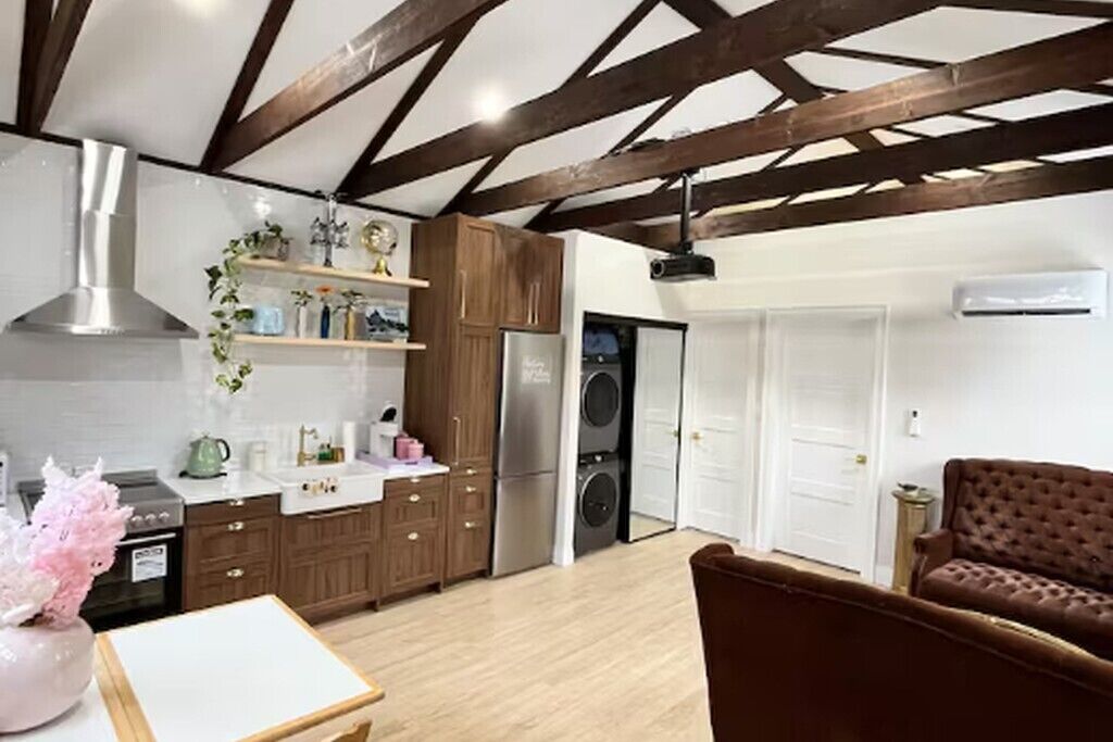 A modern kitchen with wooden beams, stainless steel appliances, and a brown leather sofa.