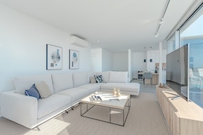 A modern living room with a sectional sofa, a coffee table, and a kitchen in the background. - Standard Villa 4 - Casangular by Upper (Adeje)