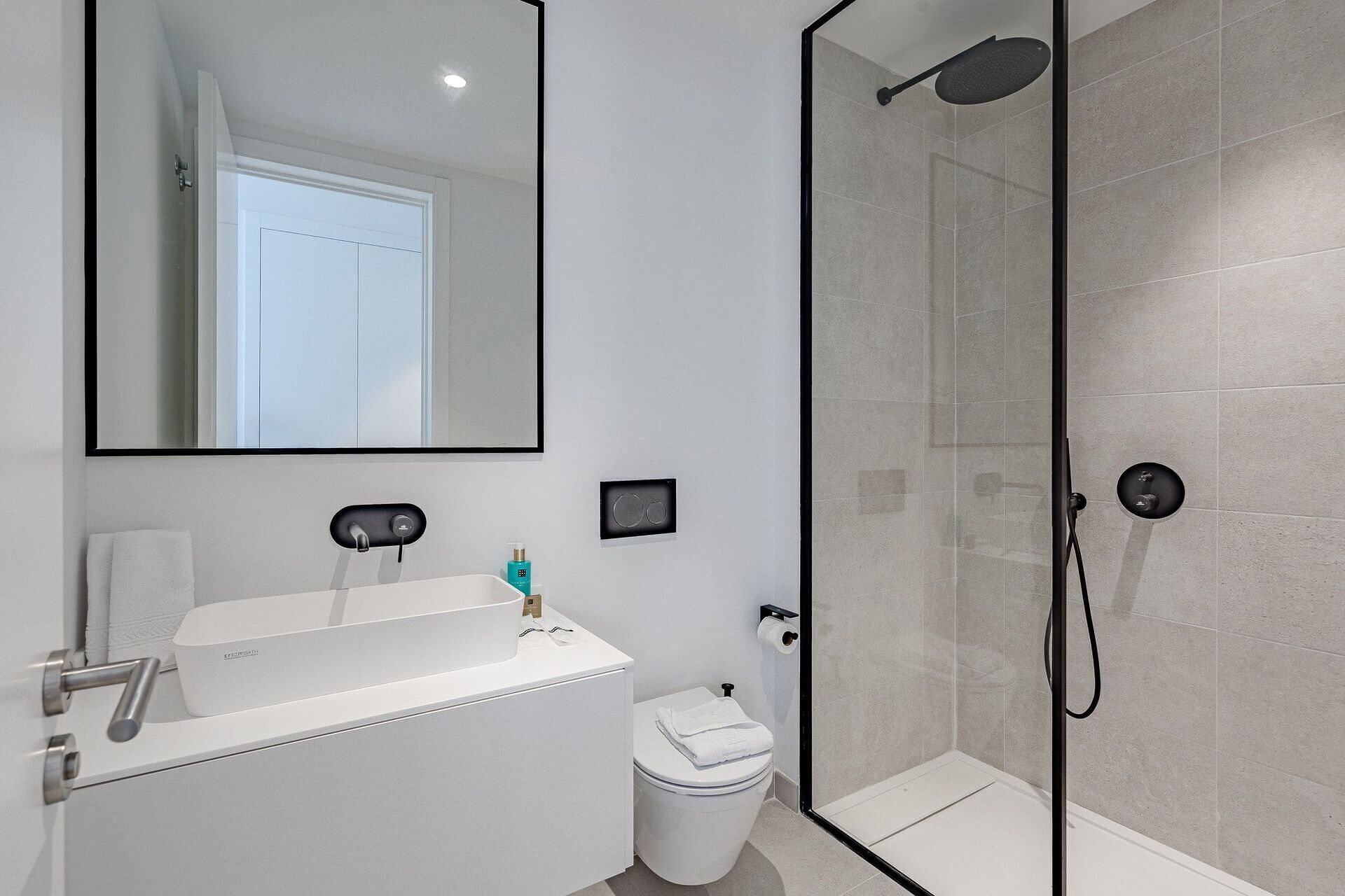 A modern bathroom with a large mirror, a sink, a toilet, and a glass-enclosed shower area.
