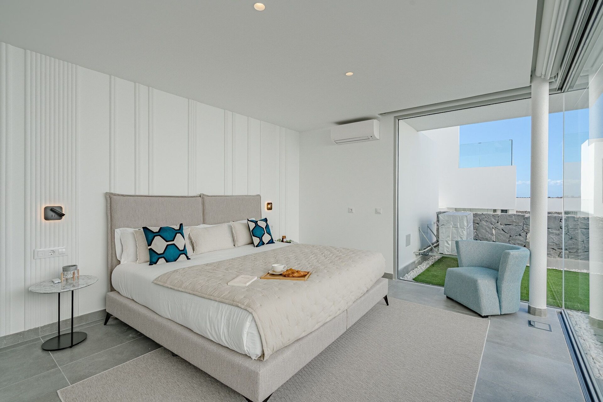 A modern bedroom with a large bed, a small side table, and a view of the outdoors.