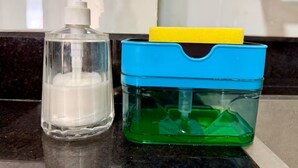 Een badkamer met een doorzichtige zeepdispenser, een zeepbakje in blauw en groen, en een gele spons.