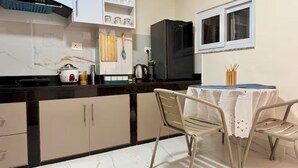 Een keuken met een zwarte koelkast, witte kasten, een marmeren aanrecht en een tafel met stoelen.