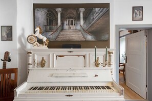 A grand piano, a large painting of a corridor, and a statue of a horse.