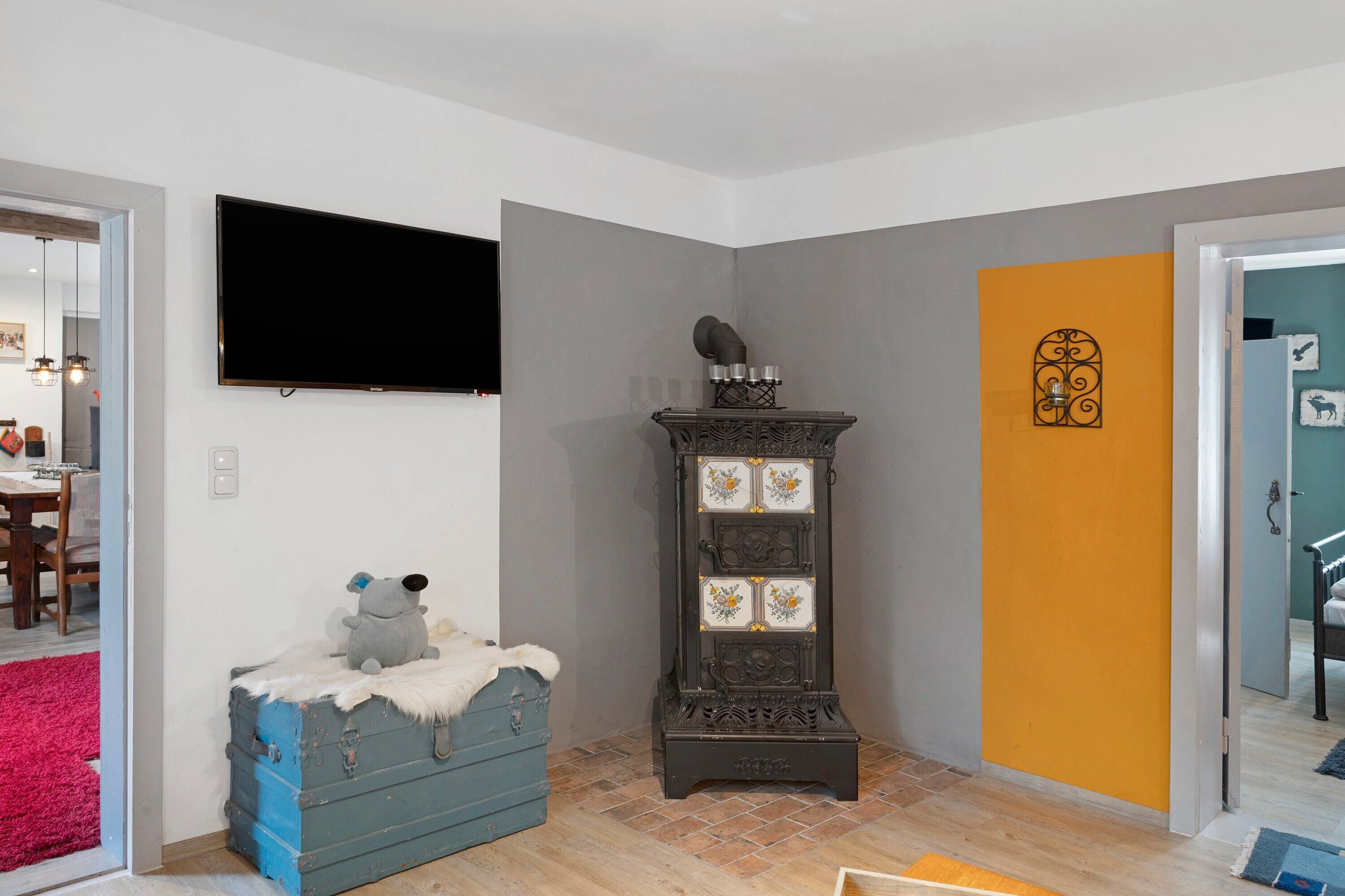 A room with a television, a blue chest of drawers, a decorative cabinet, and a door with a unique design.
