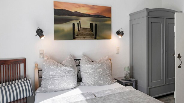 Une chambre à coucher comprenant un lit, une tête de lit, une armoire, une table de chevet, une lampe et un tableau représentant un quai.